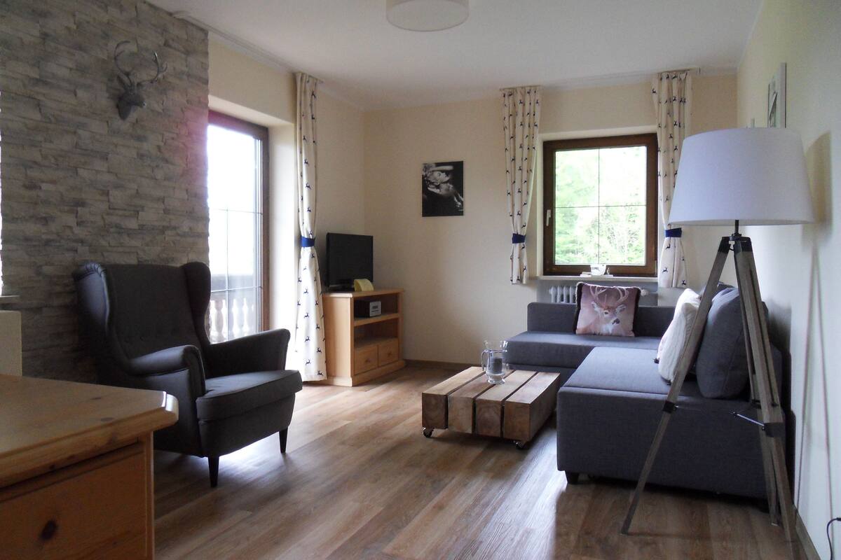 Een woonkamer met een stenen muur, een zwarte fauteuil, een grijze bank, een houten salontafel en een vloerlamp.