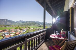 Een balkon met uitzicht op een dorp en bergen, een tafel met een vaas en een stoel.