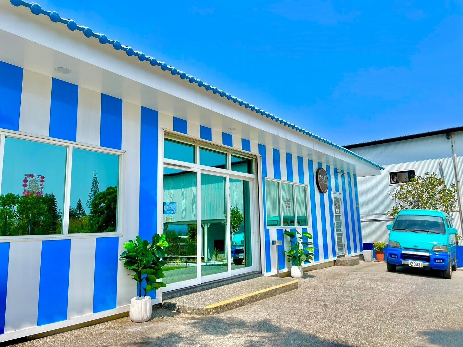 A building with blue and white vertical stripes, large windows, and a blue car parked in front.