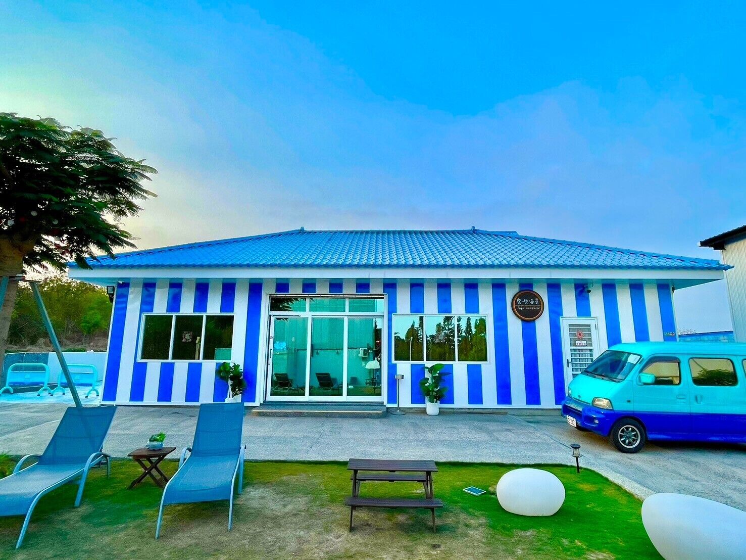 A building with a blue and white striped facade, large windows, and a blue car parked in front.