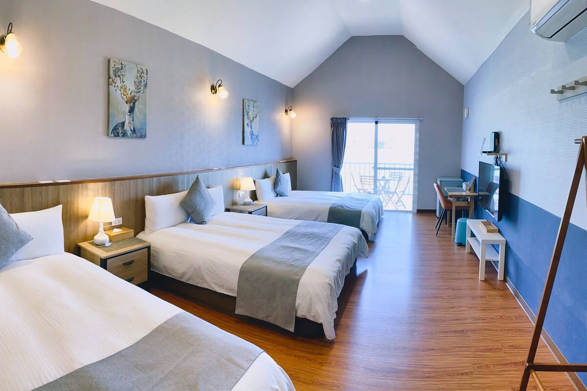 Habitación de hotel con tres camas, pisos de madera y obras de arte en las paredes.