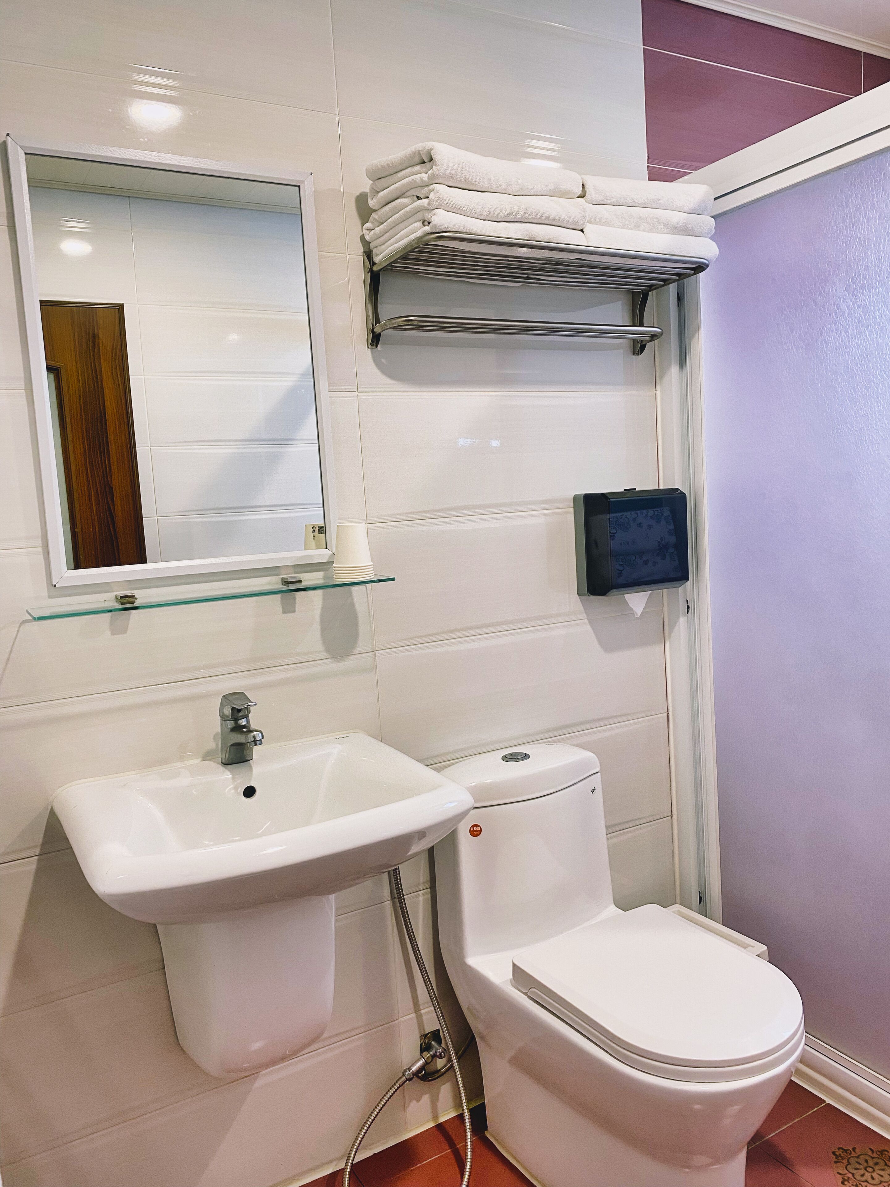 A bathroom with a white sink, toilet, and a mirror. There is a stack of white towels on a shelf above the toilet.