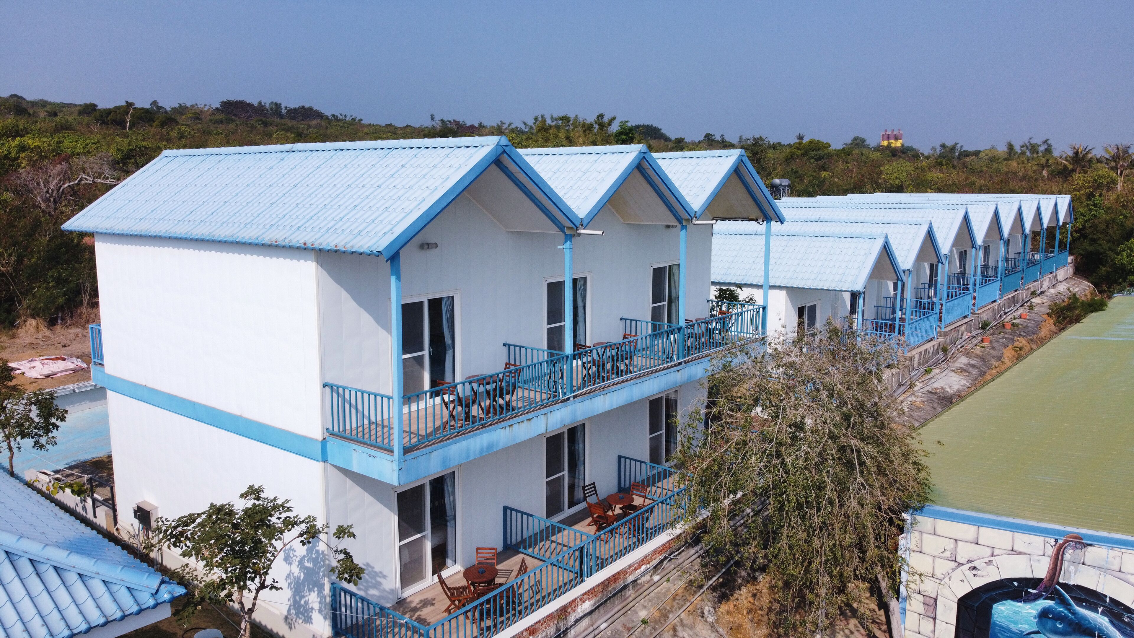 A row of blue-roofed, white buildings with balconies, situated by a body of water.