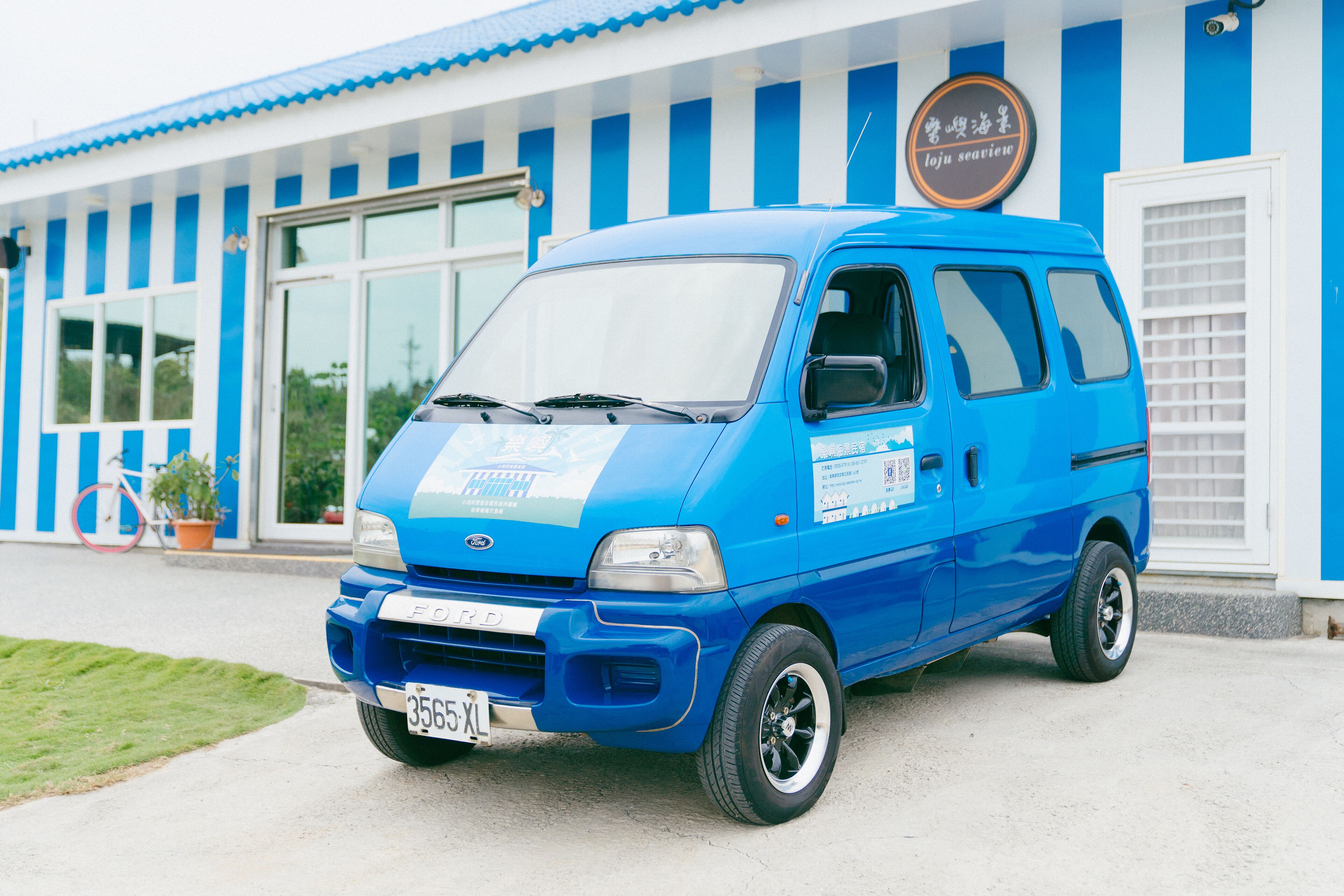 A blue van parked in front of a building with blue and white vertical stripes.