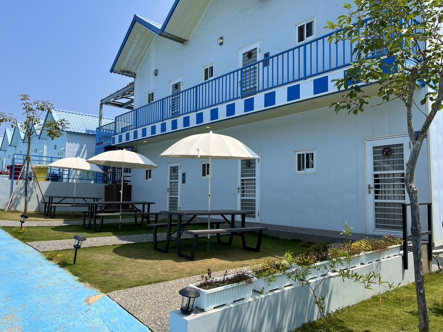A white building with blue accents, outdoor seating, and a pool.