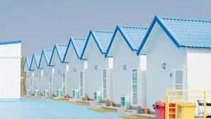 Una hilera de edificios blancos con techos azules, con puertas y ventanas, alineados a lo largo de un camino pavimentado.