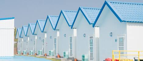 A row of blue-roofed, white buildings with doors and windows, arranged in a linear fashion along a paved walkway.