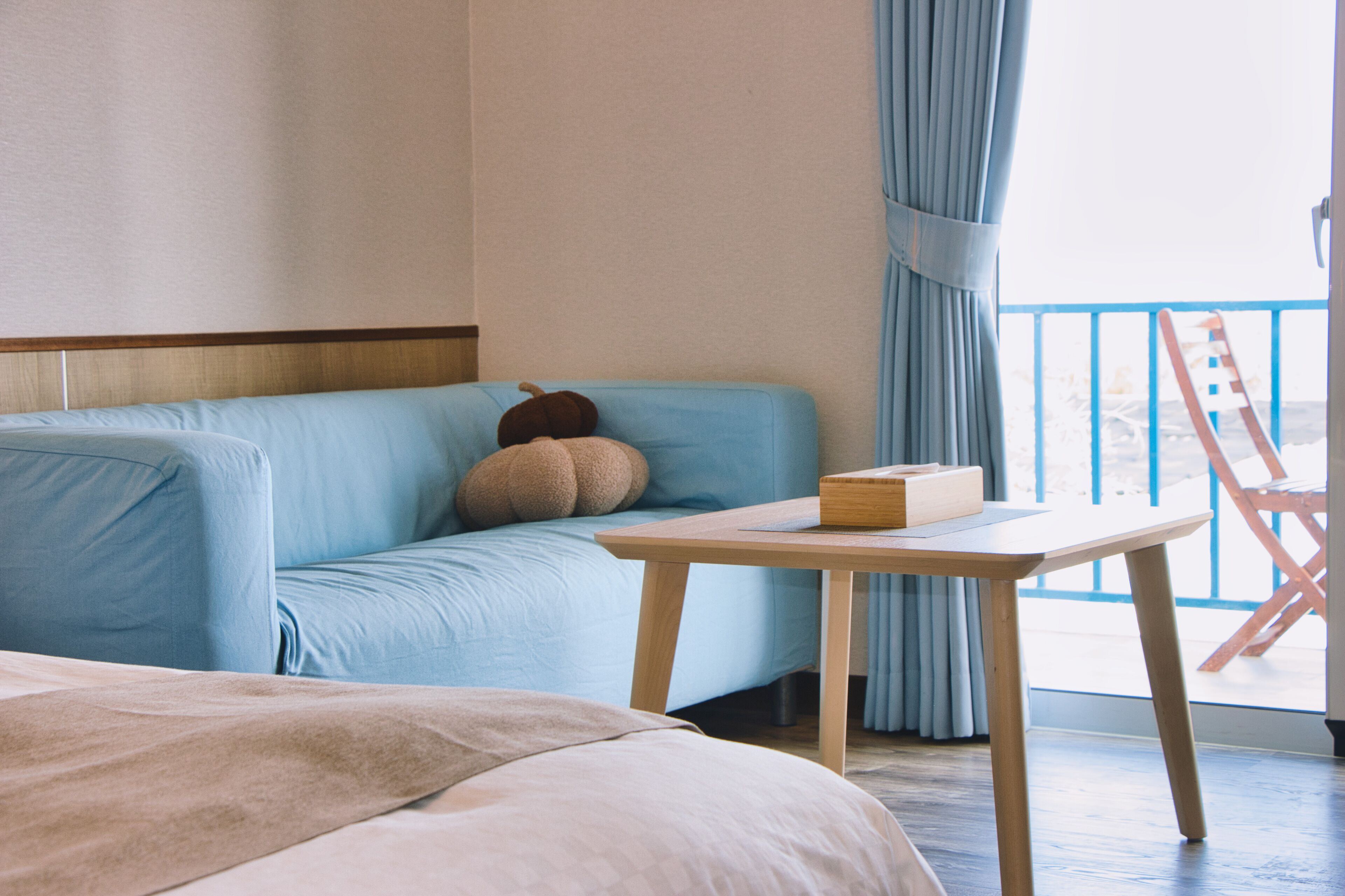 A room with a light blue sofa, a wooden table, and a view of the outside.