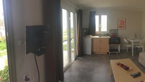 Ein kompakter Wohnbereich mit Sofa, Esstisch, Küchenzeile und einem an der Wand befestigten Fernseher.