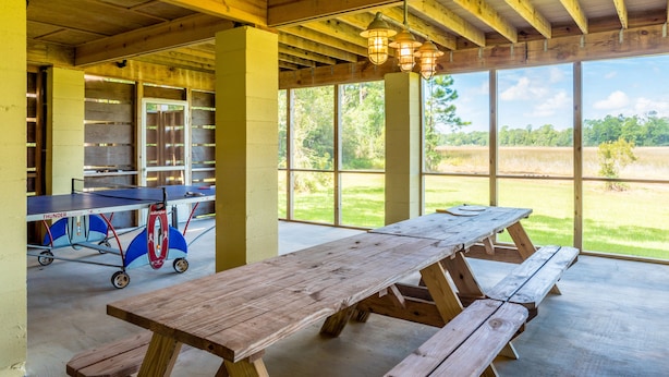An indoor picnic area with a long wooden table and benches, large windows, and a ping pong table.