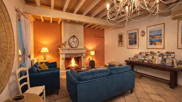 A living room with a fireplace, blue sofas, a chandelier, and framed pictures on the wall.
