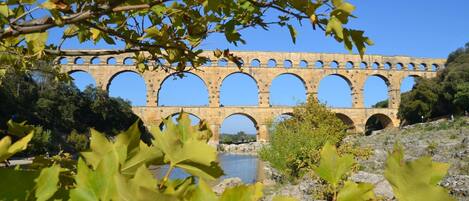 A stone aqueduct with multiple arches over a body of water, surrounded by trees and rocky terrain.