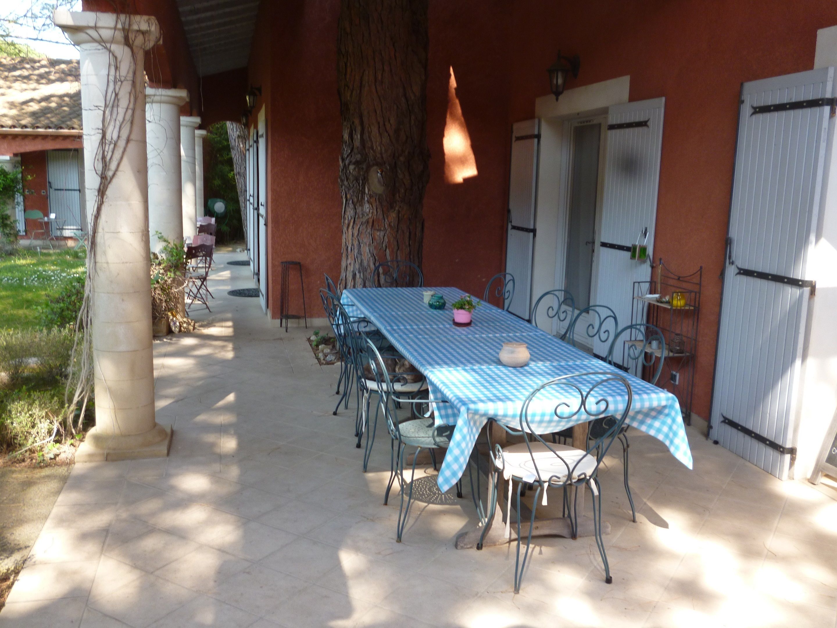 An outdoor dining area with a table covered by a blue and white checkered tablecloth, surrounded by metal chairs.