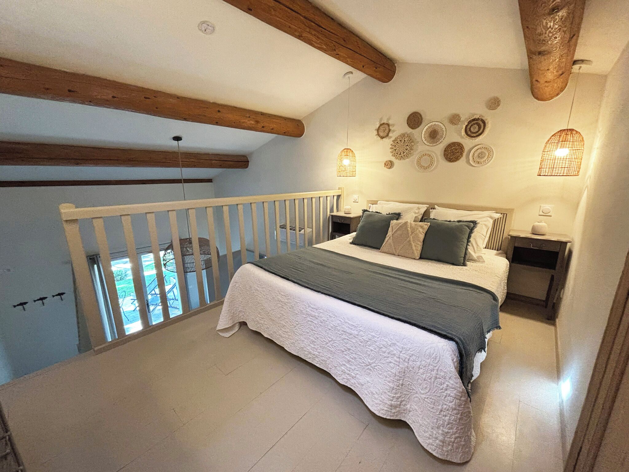 Un dormitorio con cama, mesita de noche, lámpara, barandilla y vistas al exterior.