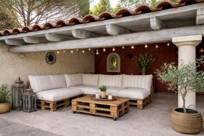 A covered outdoor seating area with a wooden bench, a round table, and potted plants. - La Bastide Des Pins (Castillon-du-Gard)