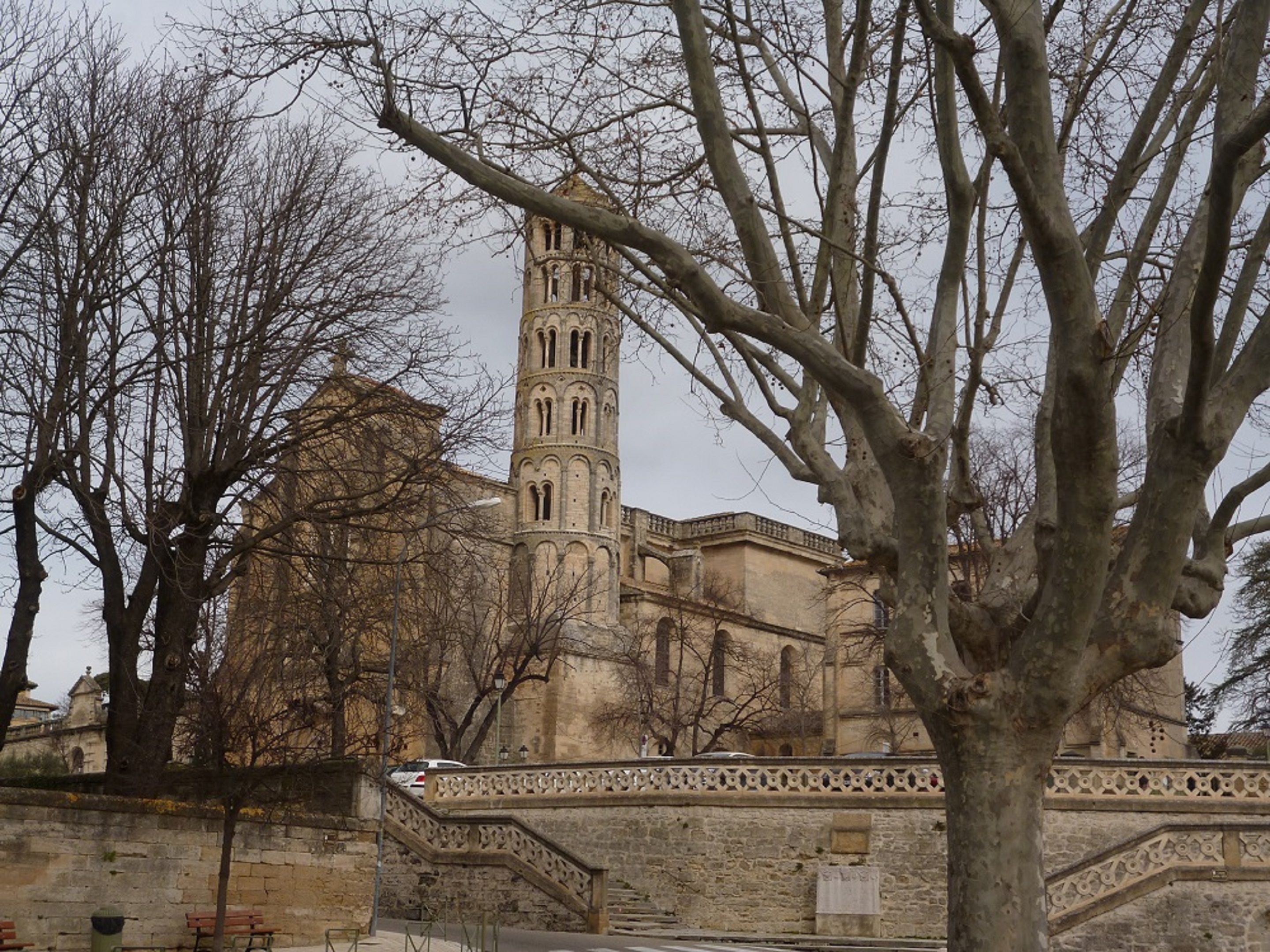 A historic building with a prominent tower, surrounded by bare trees and a stone wall.