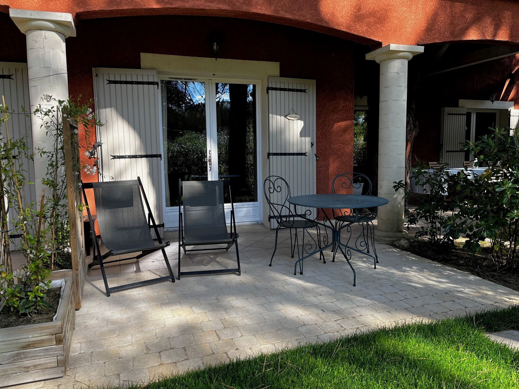 Un patio con dos sillas, una mesa, una puerta blanca y un camino de ladrillos.