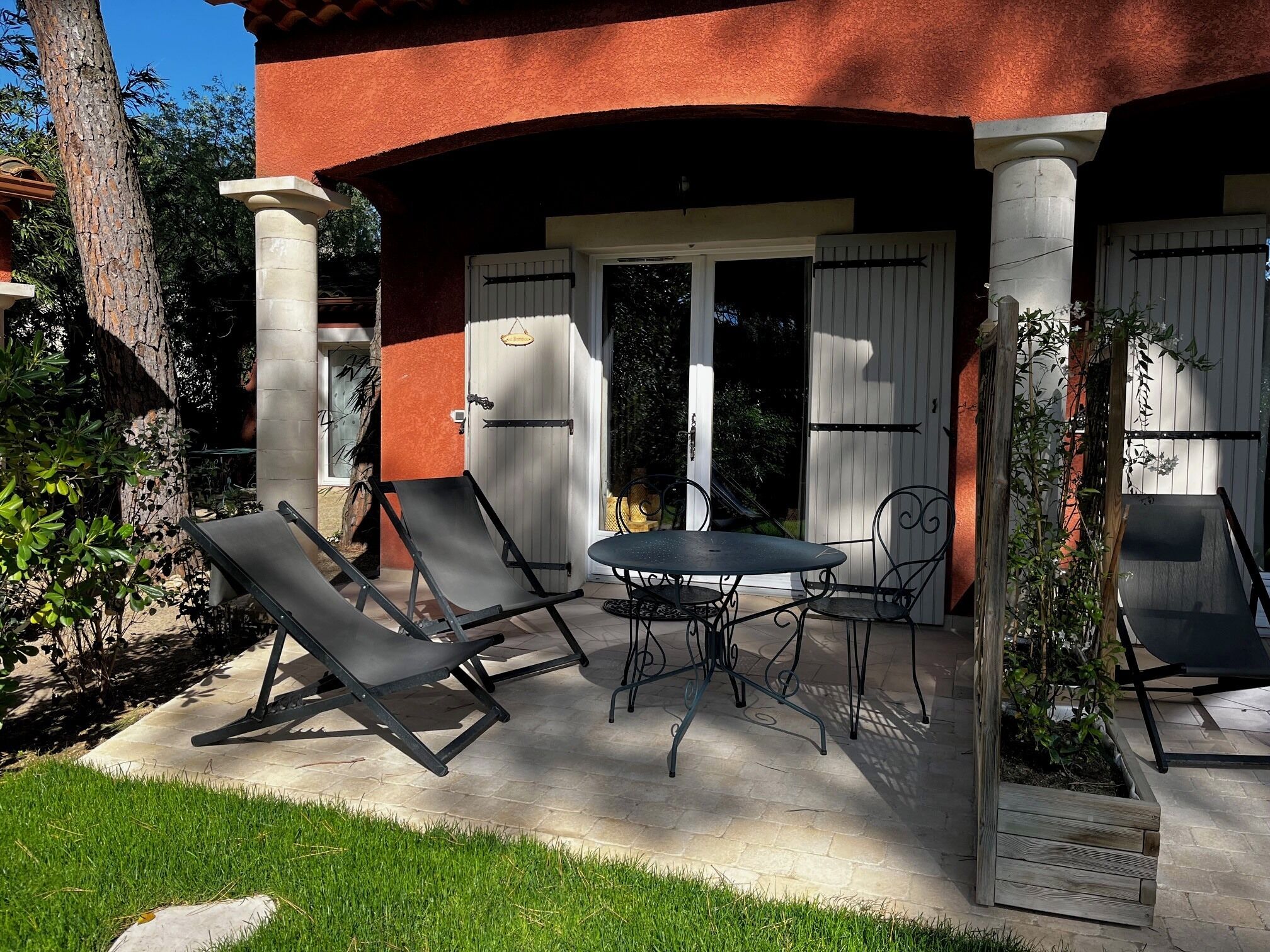An outdoor patio with a table and chairs, a covered area with a door, and a tree.