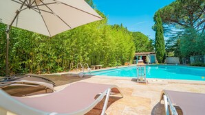 A poolside area with lounge chairs and an umbrella, surrounded by lush greenery and a clear blue sky. - La Bastide Des Pins (Castillon-du-Gard)