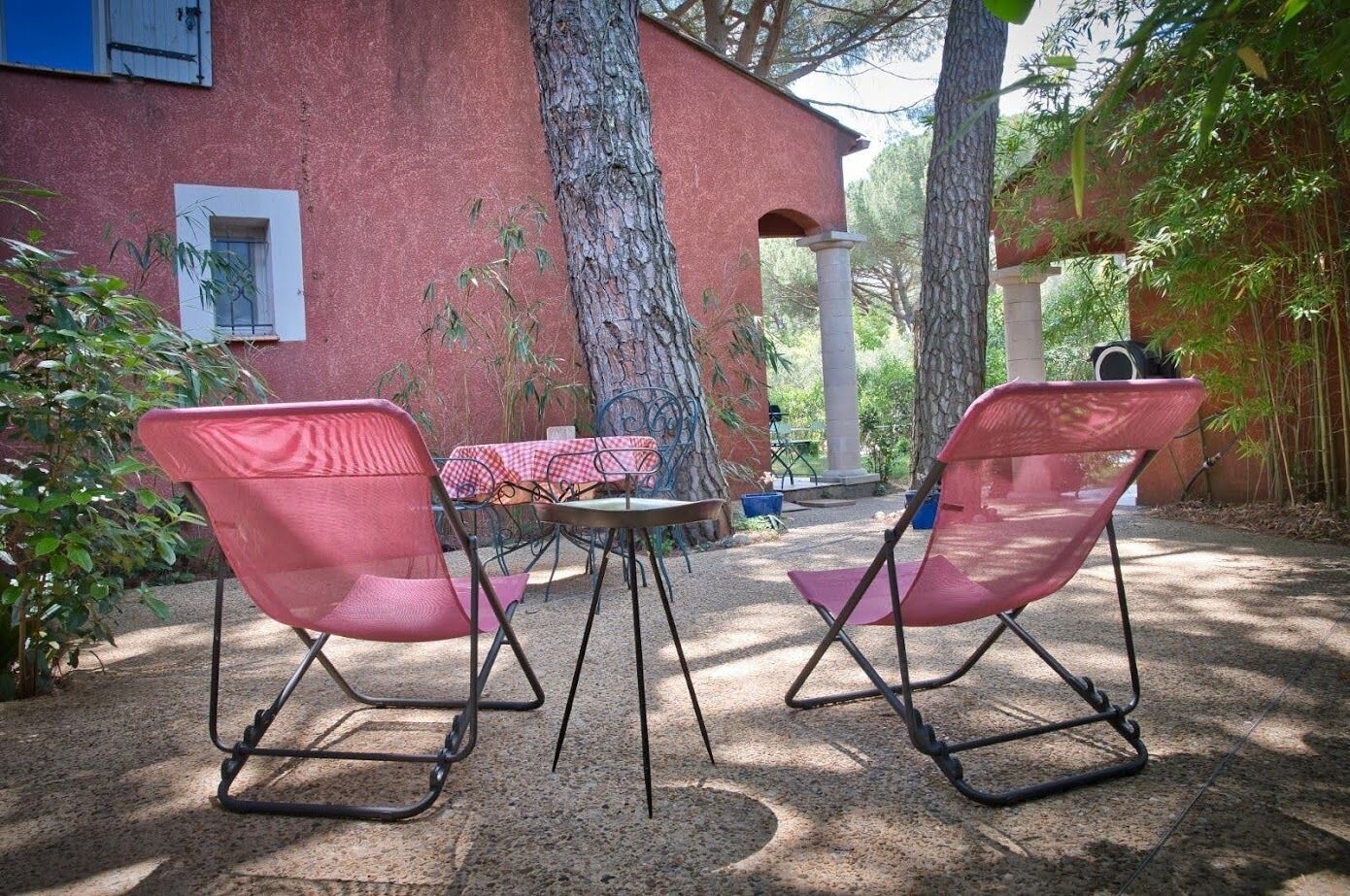 Un patio al aire libre con dos sillas rojas, una mesa redonda pequeña y un mantel a cuadros.