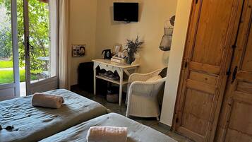 Una habitación con dos camas, una mesita con tetera y tazas, un televisor y una puerta de madera grande.