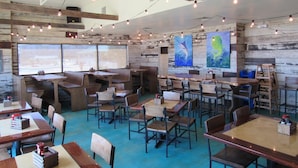A restaurant with wooden tables and chairs, string lights, and artwork on the walls.