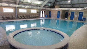 An indoor swimming pool with a hot tub, lounge chairs, and blue doors.