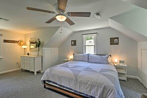 Une chambre à coucher comprenant un lit, un ventilateur de plafond, une table de chevet, une commode et une fenêtre.