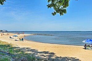 Une plage où des gens se détendent sous des parasols, une jetée en arrière-plan et une eau calme.