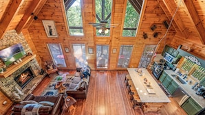 A spacious cabin interior with a fireplace, wooden floors, a dining area, and a kitchen. - Sevierville Cabin w/ Deck: Minutes to Pigeon Forge (Sevierville)