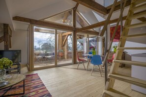 A spacious loft with a high ceiling, large windows, and a wooden staircase. - Villa Wohnlich (Oberaudorf)
