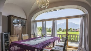 Un comedor con una mesa dispuesta para cuatro, una araña y vistas a un paisaje verde a través de amplios ventanales.