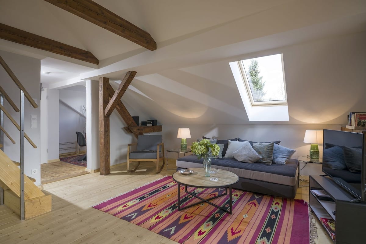 Un dormitorio tipo loft acogedor, con techo inclinado, un tragaluz grande, un sofá cama, una mesita de café y una alfombra estampada.