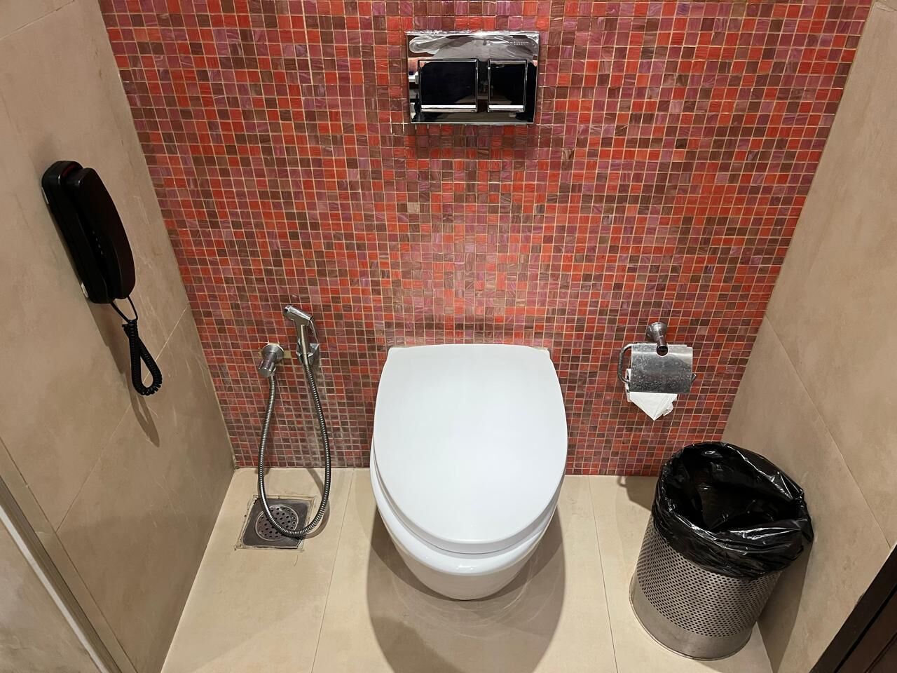 A bathroom with a white toilet, a shower, a trash bin, and a telephone.