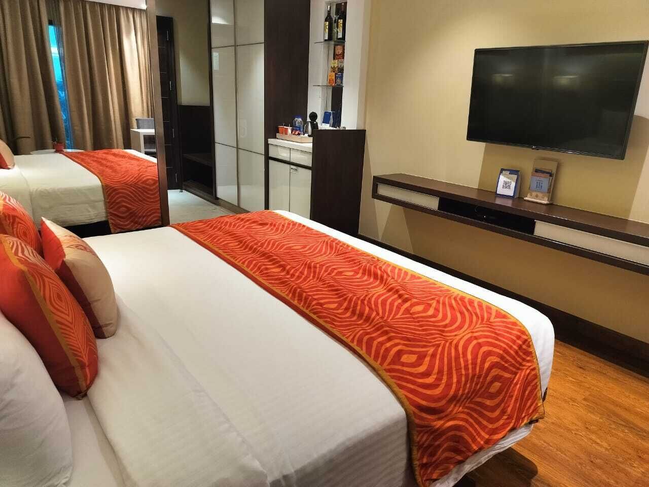 Habitación de hotel con dos camas, televisión, minibar y baño a la vista.