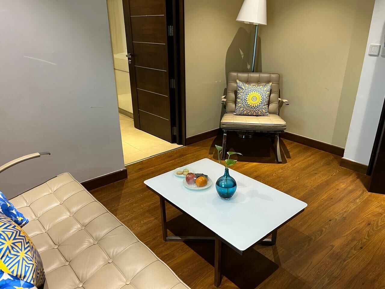 Ein modernes Wohnzimmer mit einer Couch, einem Couchtisch mit Vase und Früchten sowie einem Sessel mit gemustertem Kissen.