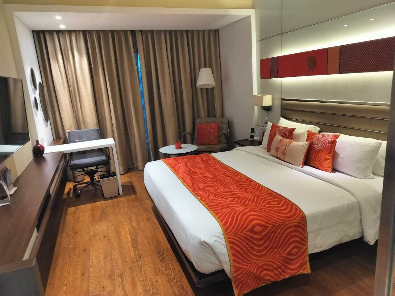 A hotel room with a bed, a desk, a chair, a TV, and a lamp.