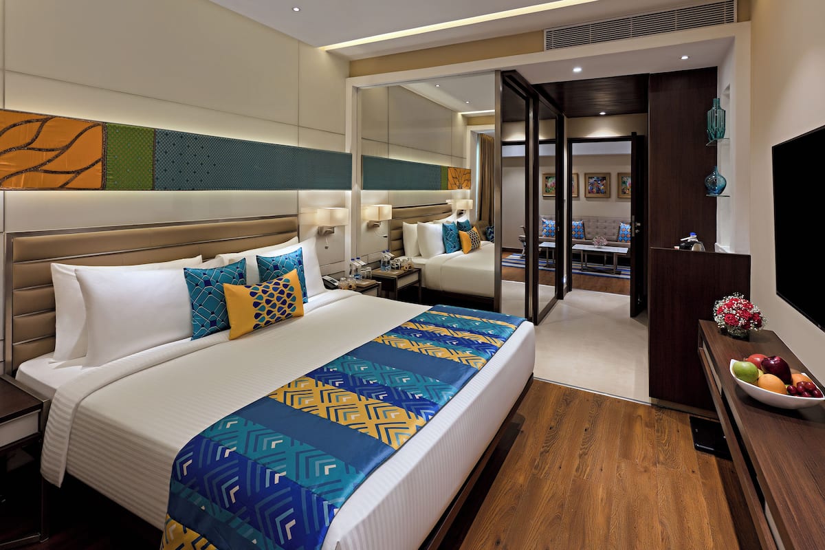 Quarto de hotel com uma cama grande, uma mesa de cabeceira, um espelho, piso de madeira e vista para a sala de jantar.