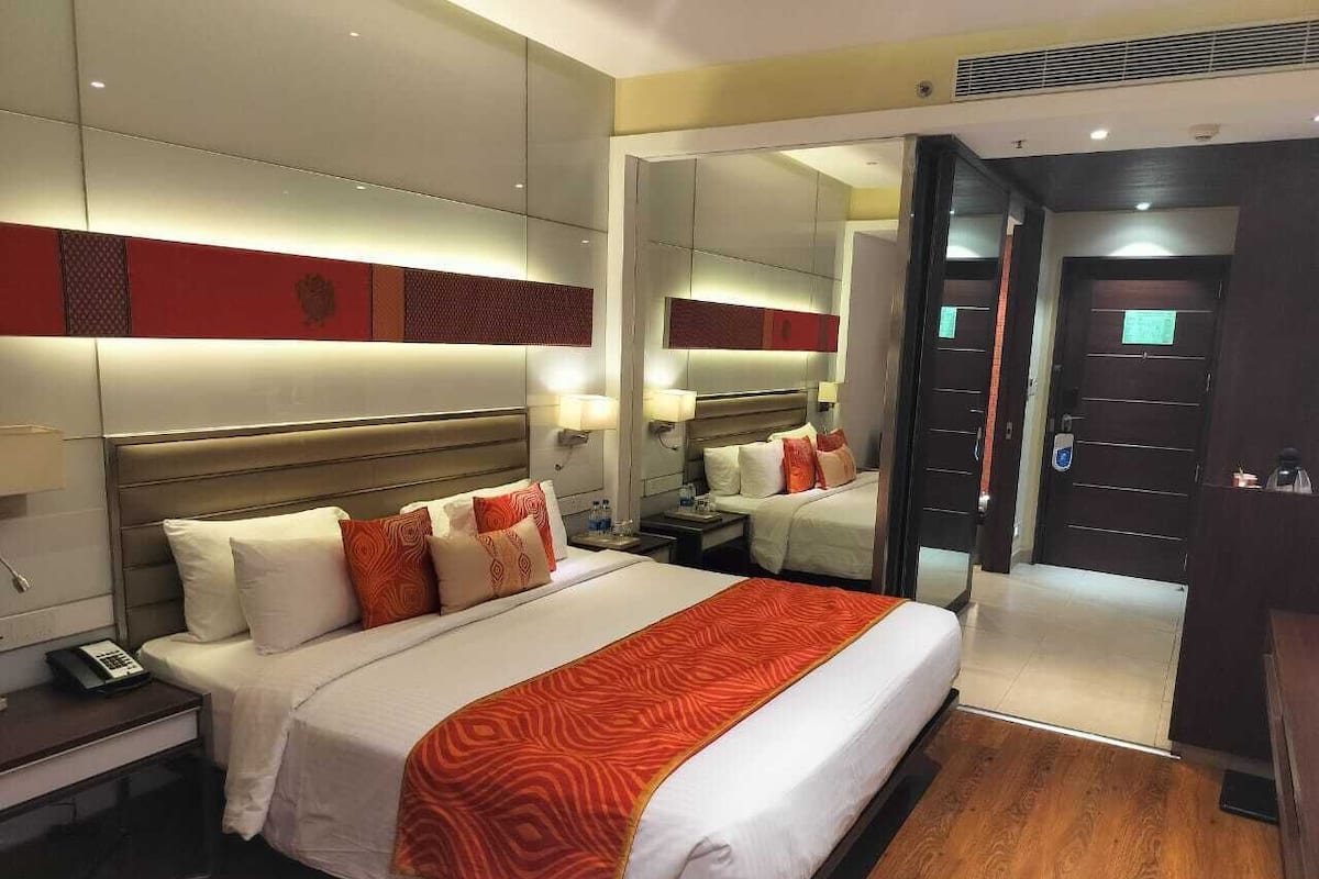 Quarto de hotel com uma cama grande, mesas de cabeceira, um espelho e um guarda-roupa.