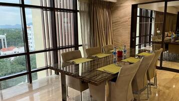 Un comedor moderno con mesa de vidrio, sillas color beige y vista a la ciudad a través de amplios ventanales.