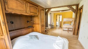 A bedroom with a wooden bed, a wooden wardrobe, and a bunk bed in the background. - Auberge De La Plaine (La Rothiere)