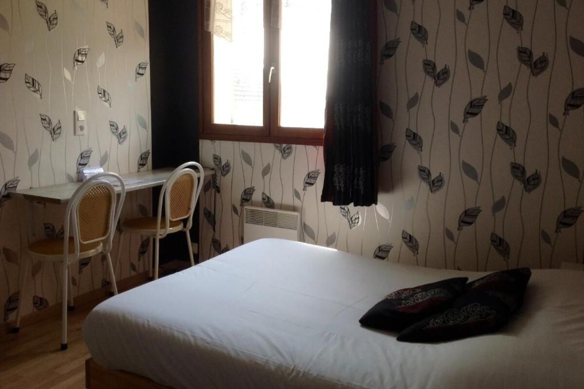 A bedroom with a bed, a desk, two chairs, and a window with curtains.