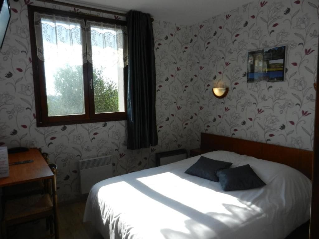 A bedroom with a bed, a desk, a window with curtains, and a wall-mounted light fixture.