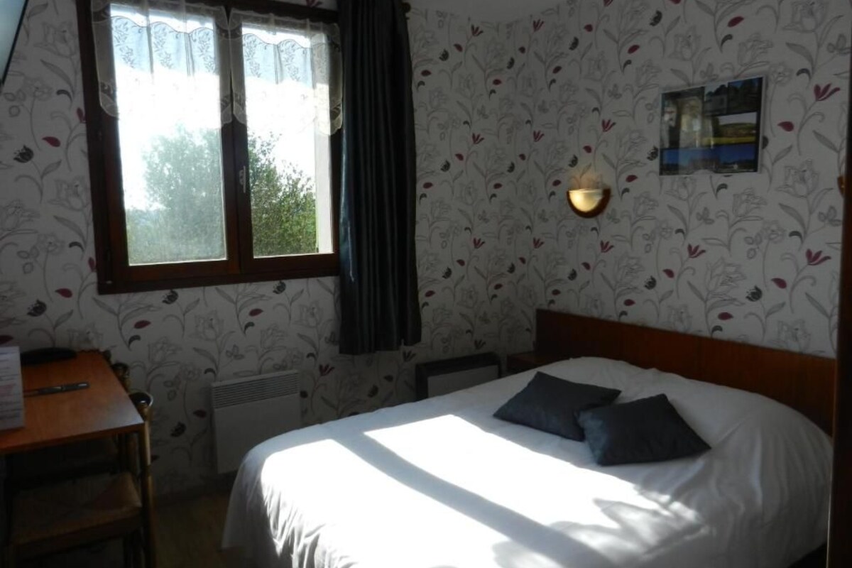 A bedroom with a bed, a desk, a window with curtains, and a wall-mounted light fixture.