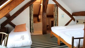 A cozy attic bedroom with two beds, wooden beams, and a view of the bathroom. - Auberge De La Plaine (La Rothiere)