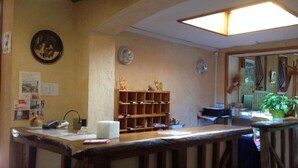 A reception area with a wooden reception desk, a bulletin board, a small shelf with decorative items, and a potted plant. - Auberge De La Plaine (La Rothiere)
