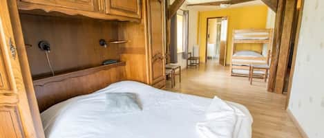 Une chambre avec un lit en bois, une armoire en bois et, au fond, un lit superposé.