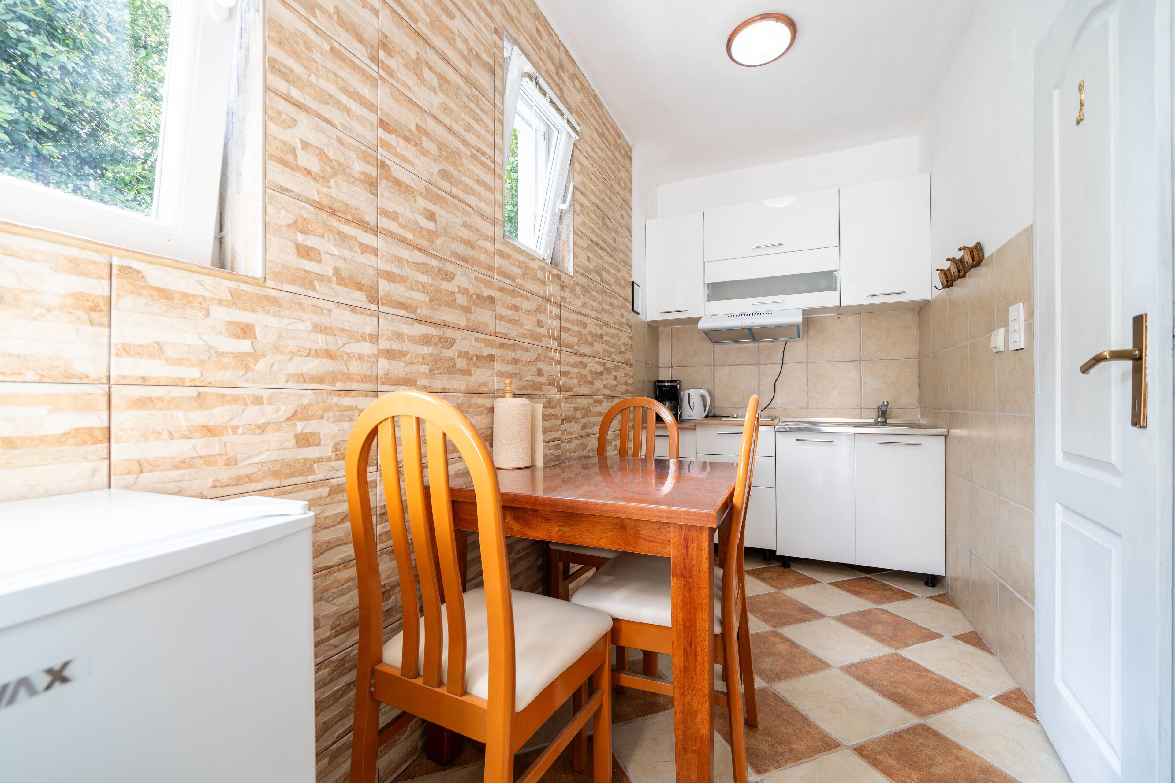 A compact kitchen with a wooden dining table, chairs, a white refrigerator, and a sink.