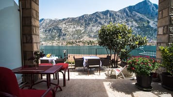 A terrace with outdoor seating, a view of a lake, and mountains in the background.