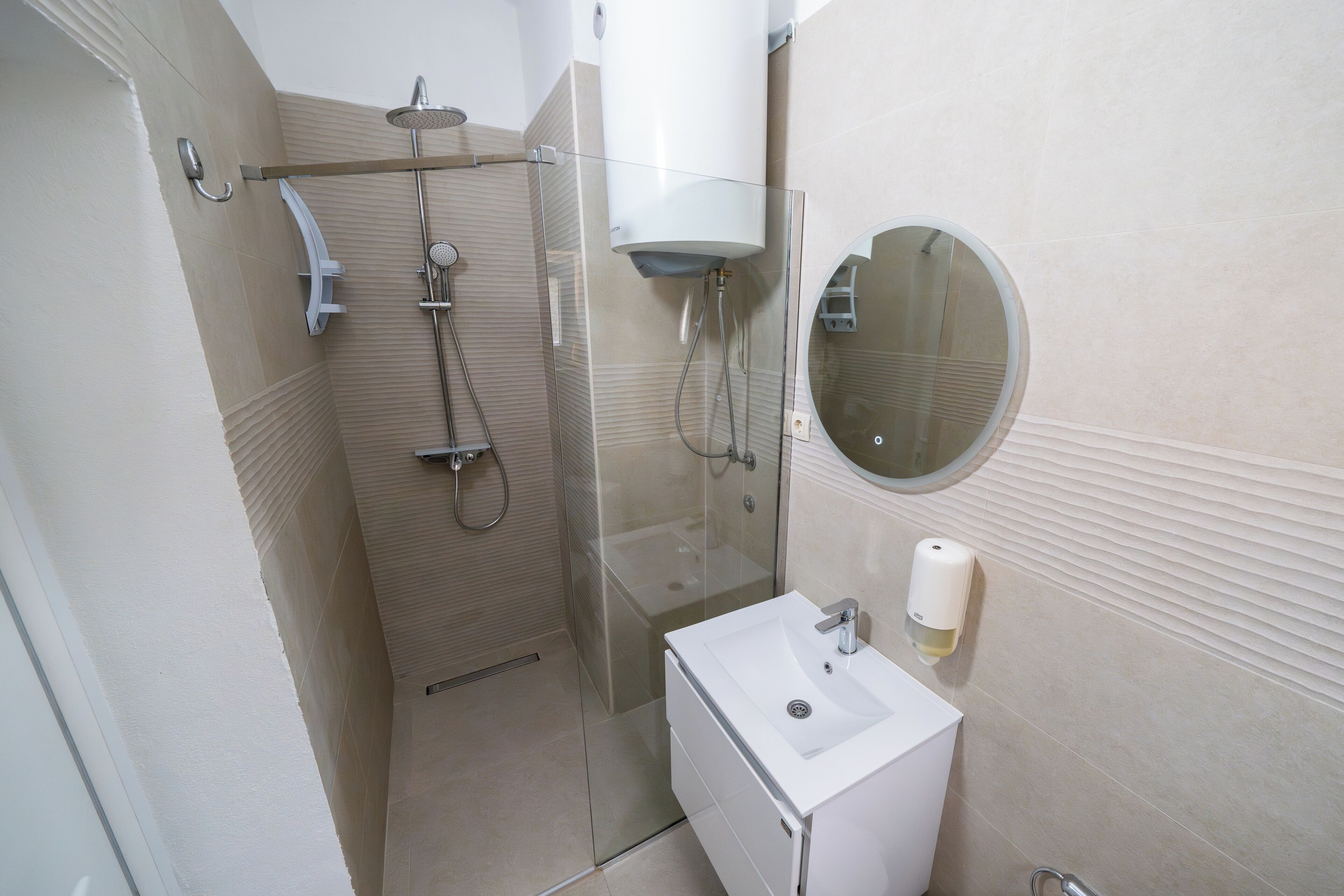 A modern bathroom with a glass-enclosed shower, a white sink, and a round mirror.